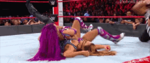 two women are wrestling in a wrestling ring and one of them has purple hair .