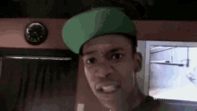 a man wearing a green hat is making a funny face in front of a television .