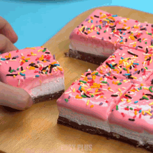 a person is taking a piece of cake with pink frosting and sprinkles from a cutting board