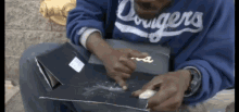a man wearing a blue dodgers sweatshirt is sitting on the ground