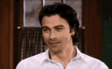 a man in a white shirt is smiling and looking at the camera in a room .