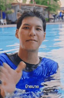 a man in a blue shirt is swimming in a pool with a foreign language behind him