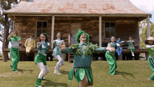 a group of people dressed in green dancing in front of a house