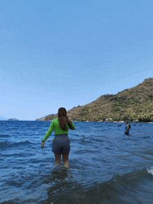 a woman in a green shirt is walking into the ocean