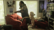 a man with a beard is standing next to a teddy bear on a couch in a living room
