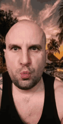 a bald man with a beard blowing a kiss in front of palm trees