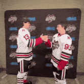 two hockey players shaking hands in front of a wall that says ghl