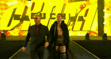 a man in a suit walks with a man in a black coat in front of a sign that says " kazuchika "
