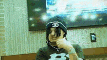 a man wearing a beanie and a necklace is sitting in front of a tv .