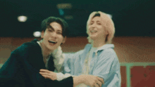 two young men are laughing and hugging each other in a room .