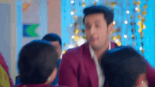 a man in a purple suit is standing in front of a group of people and talking to them .