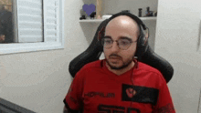 a bald man wearing glasses and headphones is sitting in a chair in front of a computer .