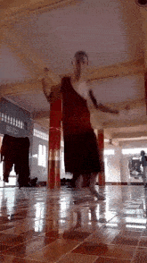 a man in a red shirt is dancing in a room with red columns