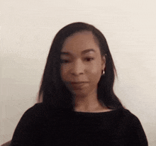 a woman wearing a black shirt and earrings looks at the camera .