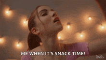 a woman is dancing in front of a string of lights and saying `` me when it 's snack time '' .
