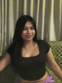 a woman in a black crop top and purple skirt is sitting on a green couch