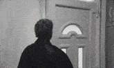 a black and white photo of a man standing in front of a white door