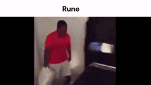 a man in a red shirt and white shorts is walking down a hallway holding a bag .