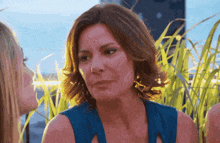 a woman in a blue dress is talking to another woman in a field of tall grass
