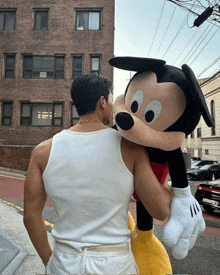 a man in a white tank top is holding a mickey mouse stuffed animal