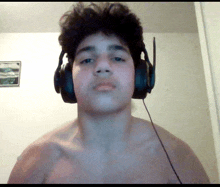 a shirtless young man wearing headphones and a picture on the wall behind him