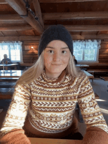 a woman wearing a sweater and a hat is smiling for the camera