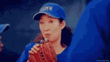a woman in a blue baseball cap is drinking from a glove .