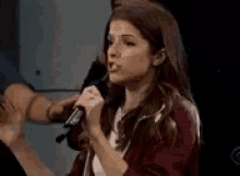 a woman is singing into a microphone while standing in front of a group of people .