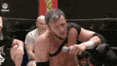 a man is holding a microphone in a wrestling ring while a group of people watch .