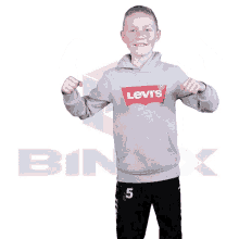 a boy wearing a grey levi 's hoodie flexing his muscles
