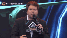 a man is holding a microphone in front of a screen that says eltrecetv.com on it