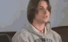 a young man in a hoodie is sitting on a couch eating a french fry .