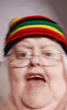 an elderly woman wearing glasses and a colorful hat makes a funny face