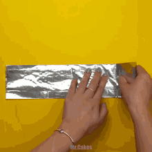 a person is holding a piece of aluminum foil on a yellow background with the words mr.cakes below them