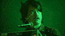 a man with a mustache is singing into a microphone in front of a green background .