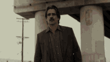 a man with a mustache and glasses stands in front of a bridge