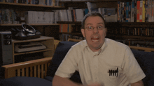 a man sitting on a couch with his mouth open and a pen in his pocket that says 4444