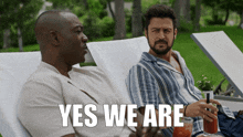 two men are sitting on lawn chairs with the words yes we are behind them