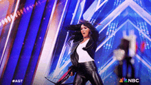 a woman is holding a bow and arrow on a stage with a nbc logo in the background