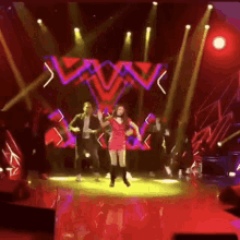 a woman in a red dress is dancing on a stage with other people .