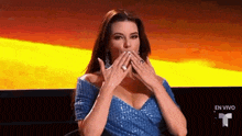a woman in a blue dress is blowing a kiss while sitting on a couch .