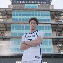a young man wearing a butler jersey stands in front of a scoreboard