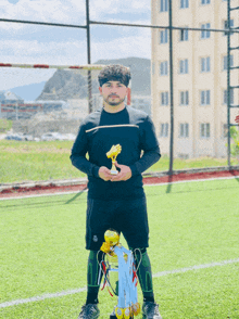a man holding a trophy on a soccer field with a building in the background