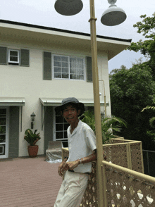 a man wearing a hat stands on a balcony in front of a house