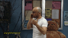 a man standing next to a teddy bear in front of a bulletin board with a sign that says " holiday joy "