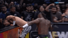 two men are wrestling in front of a crowd and one of them is laying on the ground .