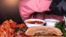 a woman in a pink hoodie is eating a large piece of meat