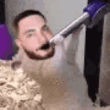 a man with a beard is holding a vacuum cleaner in his mouth while standing in the sand .