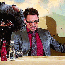 a man in a suit and tie is sitting at a table with bottles of water