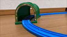a toy train is going through a green tunnel on a wooden floor